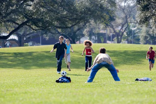 Children playing soccer together on a neighborhood lawn